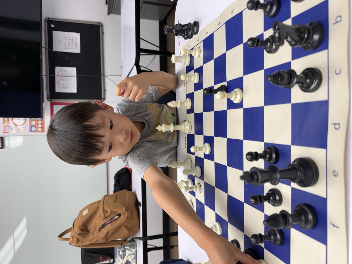 A young student reaching to move a chess piece during a lesson