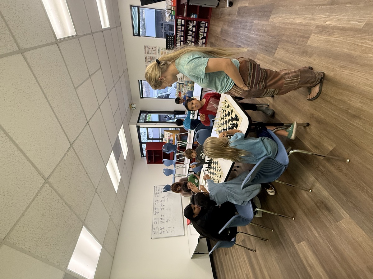 A coach checking in with students gathered around a chess table